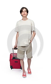 A teenage boy in a T-shirt and shorts walks with a red suitcase on wheels, isolated on a white background