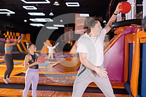 Teenage boy throwing ball in basket high jumping in trampoline arena