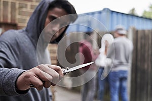 Teenage Boy In Urban Gang Pointing Knife Towards Camera