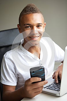 Teenage Boy Using Laptop And Mobile At Home