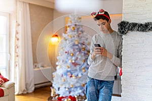Teenage boy using mobile phone at home in Christmas time