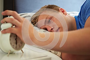 Teenage Boy Waking Up In Bed And Turning Off Alarm Clock