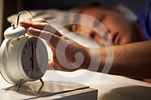 Teenage Boy Waking Up In Bed And Turning Off Alarm Clock