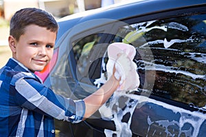 Teenage boy washing a car on a sunny day