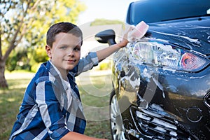 Teenage boy washing a car on a sunny day