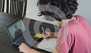 Teenage boy watches lesson on laptop during remote schooling