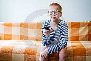 A teenage boy watches tv, using remote control to change channels. Young man