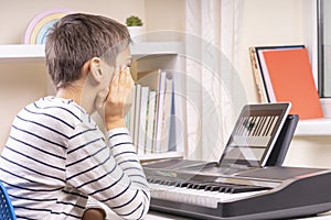 Boy watching video lesson at tablet computer and learing playing digital piano at home. Online learning remote education