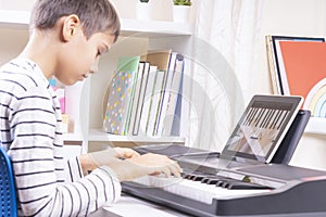 Teenage boy watching video lesson at tablet computer and playing digital piano at home. Online learning remote education