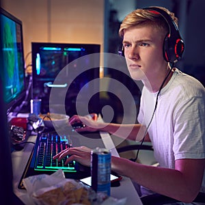 Teenage Boy Wearing Headset Gaming At Home Using Dual Computer Screens