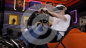 A teenage boy wearing virtual reality glasses sits in a car driving simulator.