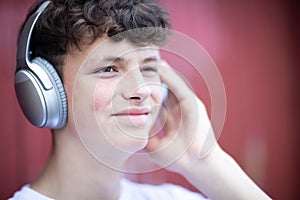 Teenage Boy Wearing Wireless Headphones And Listening To Music In Urban Setting