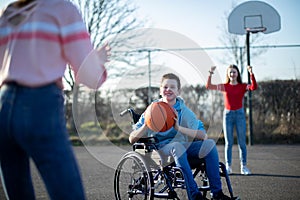 Teenage Boy In Wheelchair Playing Basketball With Friends