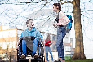 Teenage Boy In Wheelchair Talking With Female Friend As They Leave High School