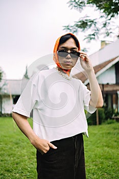 a teenage boy in a white shirt wearing sunglasses and a bandana in front of a house