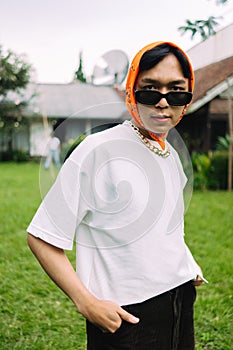 a teenage boy in a white shirt wearing sunglasses and a bandana in front of a house