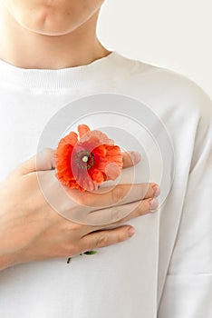 Teenage boy in white t-shirt holding hand with red poppy on chest near heart. Symbol of Remembrance day, Armistice day