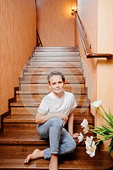 a teenage boy in a white T-shirt and jeans with a bouquet on a wooden staircase