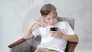 A teenage boy in a white T-shirt with a smartphone in his hand.