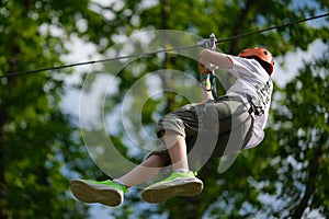 Teenage boy on zipline having fun at outdoor extreme adventure park. Active childhood, playing outdoors.