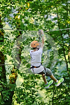 Teenage boy on zipline having fun at outdoor extreme adventure park. Active childhood, playing outdoors.