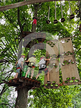 Teenage boys are climbing on a hanging rope park in trees on an obstacle course