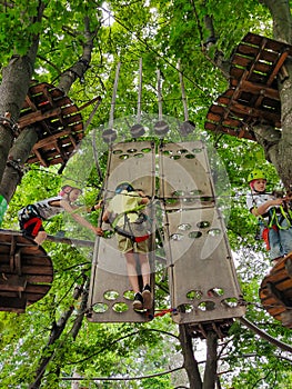 Teenage boys are climbing on a hanging rope park in trees on an obstacle course