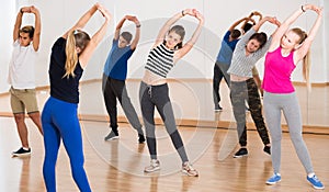 Teenage boys and girls with trainer stretching in dance hall