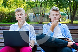 Teenage Boys On Park Bench Using Laptop And Digital Tablet