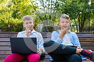 Teenage Boys On Park Bench Using Laptop And Digital Tablet