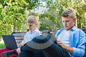 Teenage Boys On Park Bench Using Laptop And Digital Tablet