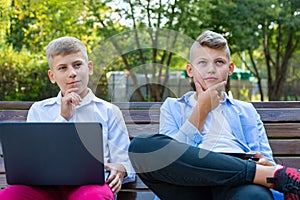 Teenage Boys On Park Bench Using Laptop And Digital Tablet