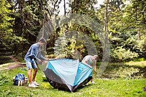 Teenage boys pitching a tent at the lake in forest.