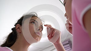 Teenage brunette approaches large mirror and pops zits