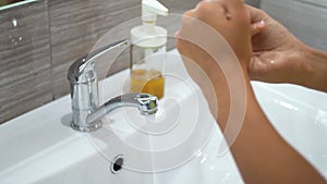 A teenage child opens the tap and washes his hands with soap under running water in sink. Clean your hands to prevent