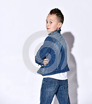 Teenage child in t-shirt, blue jeans, denim jacket. He standing by his back to the camera, looking back, posing isolated on white