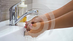 A teenage child washes his hands with soap under running water in the sink and then turns off the tap. Clean your hands