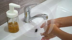 A teenage child washes his hands with soap under running water in the sink and then turns off the tap. Clean your hands