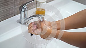 A teenage child washes his hands with soap under running water in the sink and then turns off the tap. Clean your hands