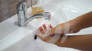 A teenage child washes his hands with soap under running water in the sink and then turns off the tap. Clean your hands