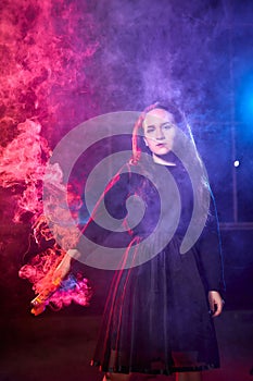 Teenage chubby girl with colored smoke torch in hand during photoshoot with colored smoke at night and black background