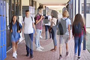 Teenage classmates stand talking in school hallway