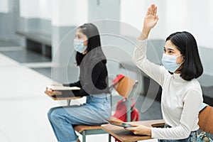 Teenage college students sitting in the class and raising hand up to participate ask question during lecture. High school student