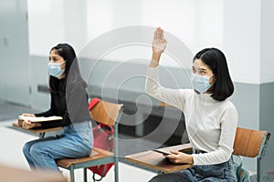 Teenage college students sitting in the class and raising hand up to participate ask question during lecture. High school student