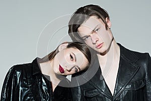 Teenage couple in love wearing black leather jackets isolated on gray background. Stylish brunette girl leaning on her