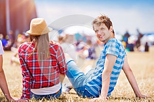 Teenage couple at summer music festival, sitting in front of sta