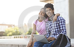 Teenage couple using laptop outdoors posing to camera