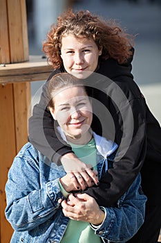 Teenage daughter hugging her mother, outdoor portrait on a sunny day