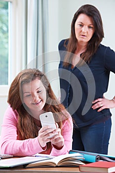 Teenage Daughter Using Mobile Phone Whilst Studying