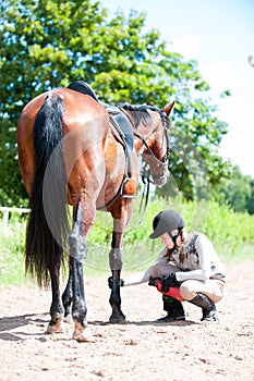 Teenage equestrian girl checking for injury of bay horse leg